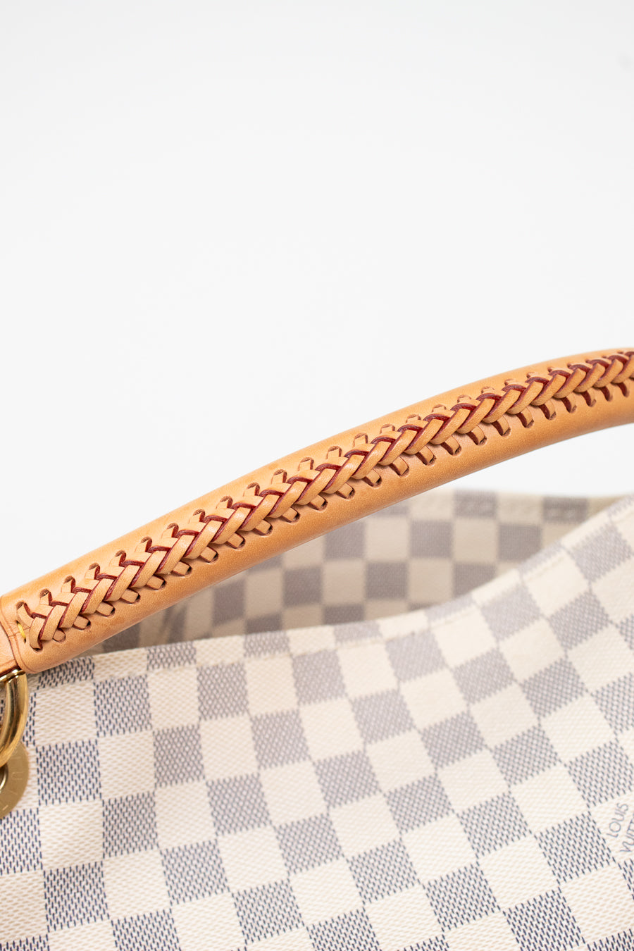 Close-up of a handbag handle made of light tan leather with a braided stitch pattern, attached to a gray and white checkered canvas body.