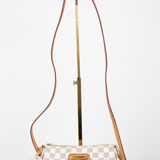 A Louis Vuitton shoulder bag in Damier Azur canvas with a brown leather strap and gold-tone hardware, displayed on a stand against a white background.