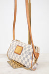 A small crossbody handbag with a gray and white checkerboard pattern, tan leather trim, and a gold-tone chain strap, displayed on a stand against a light background.