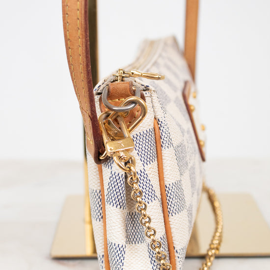A close-up side view of a Louis Vuitton shoulder bag in Damier Azur canvas, featuring a beige and blue checkered pattern, tan leather trim, and a gold-tone chain strap.
