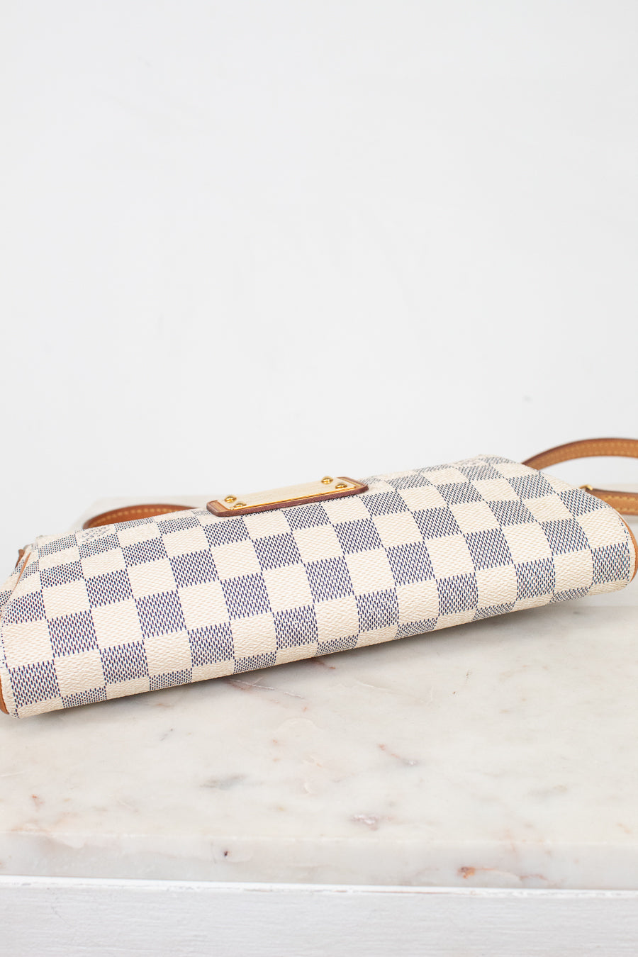 A Louis Vuitton shoulder bag in the Damier Azur canvas, featuring a cream and light blue checkered pattern with tan leather trim and a gold-tone turn-lock clasp, showing the bottom on a white marble surface.