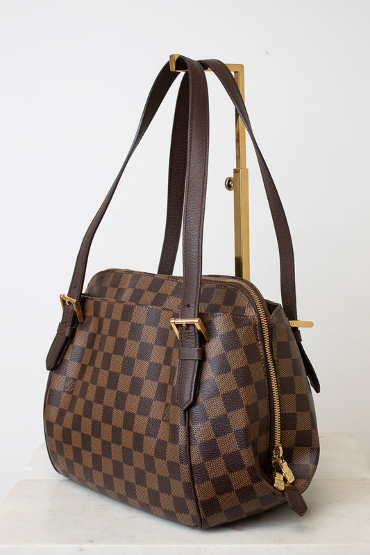 A brown checkerboard handbag with dark brown leather straps and gold-tone hardware, displayed on a white surface against a white background.