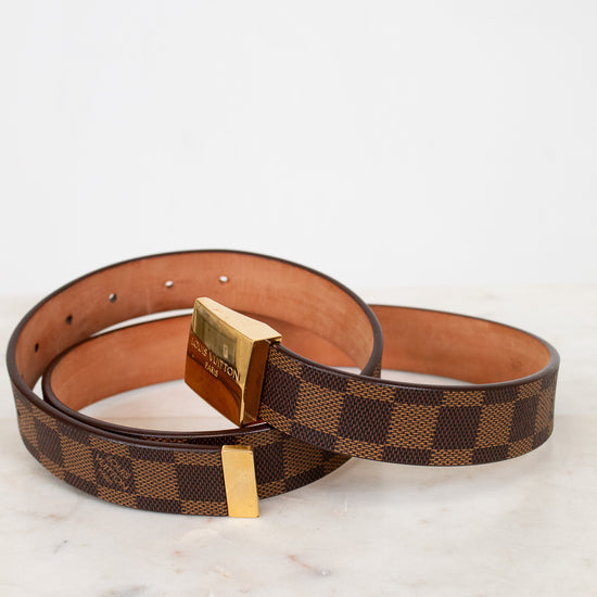 Brown checkered belt with gold buckle on a white marble surface