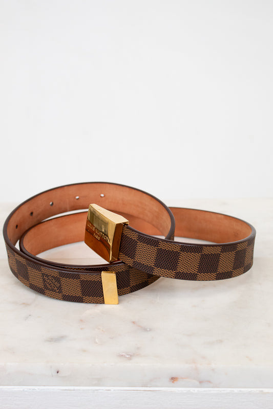 Brown checkered belt with gold buckle on a white marble surface