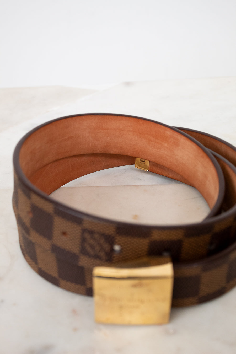 Brown checkered belt with gold buckle on a light background