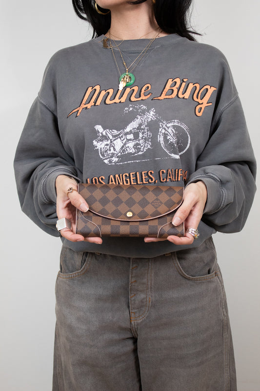 Person wearing a gray sweatshirt with text and graphic, holding a brown coated canvas wallet.