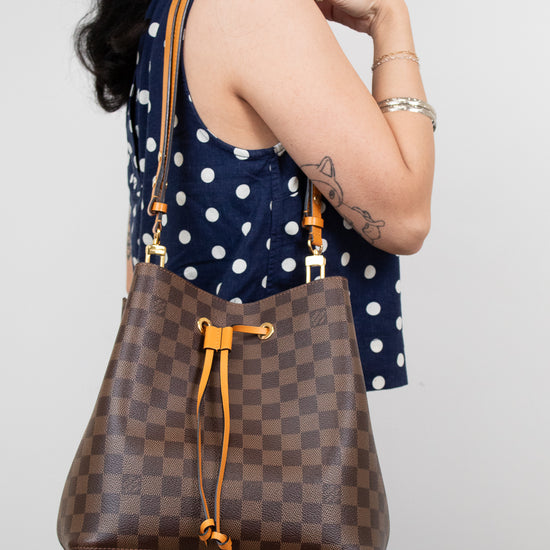 Woman holding a brown checkered handbag with orange accents against a plain background