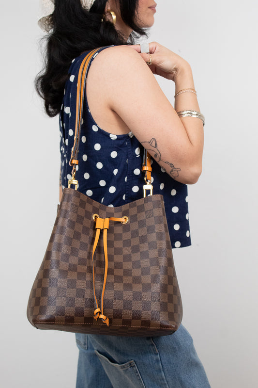 Woman holding a brown checkered handbag with orange accents against a plain background