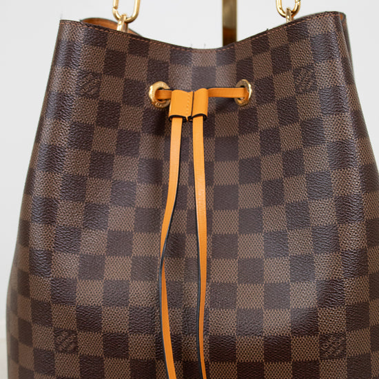 Brown checkered handbag with orange leather straps on a white background
