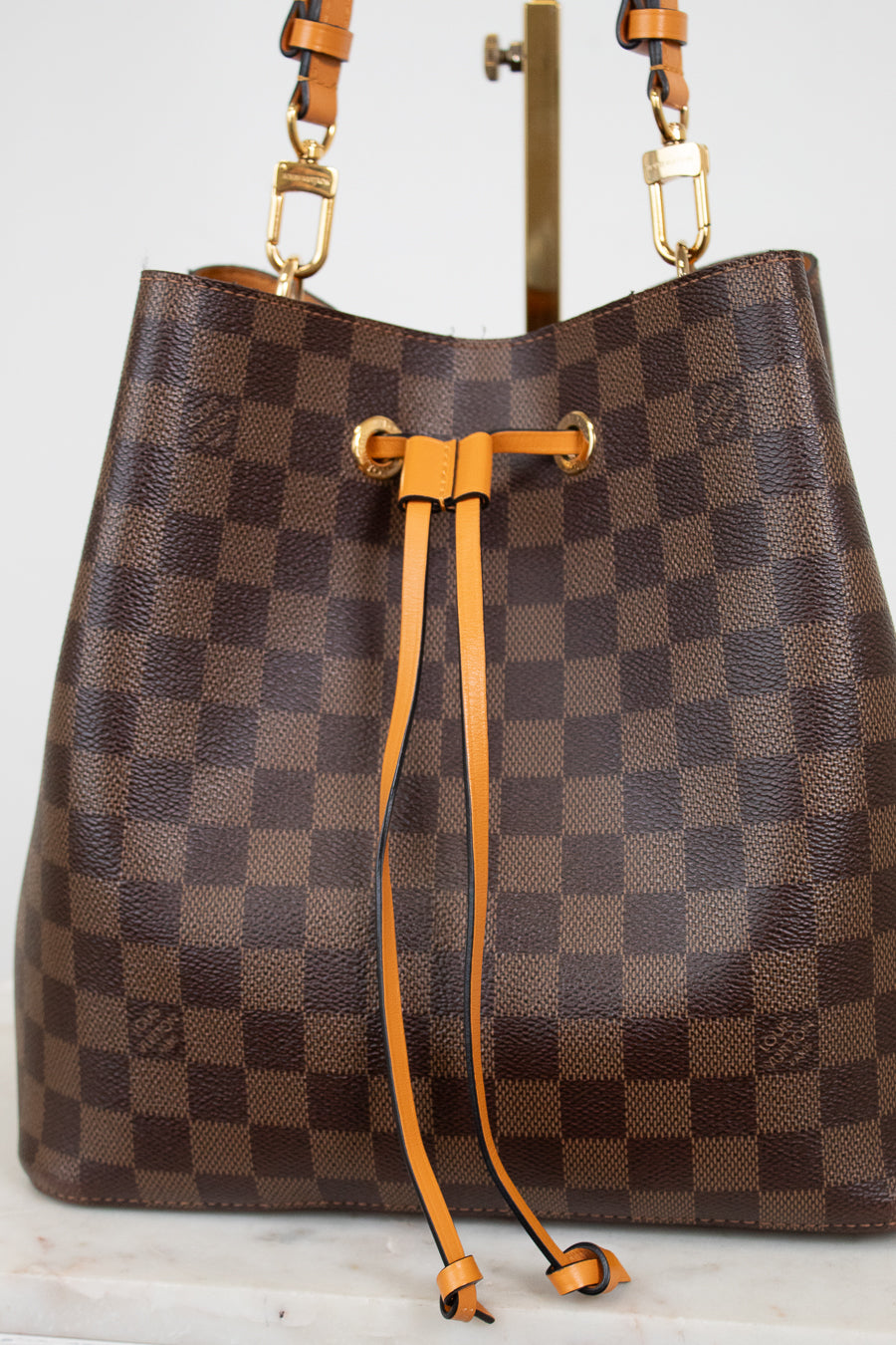 Brown checkered handbag with orange leather straps on a white background