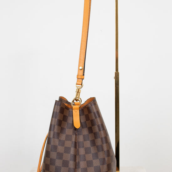 Brown checkered handbag with orange leather strap on a white background