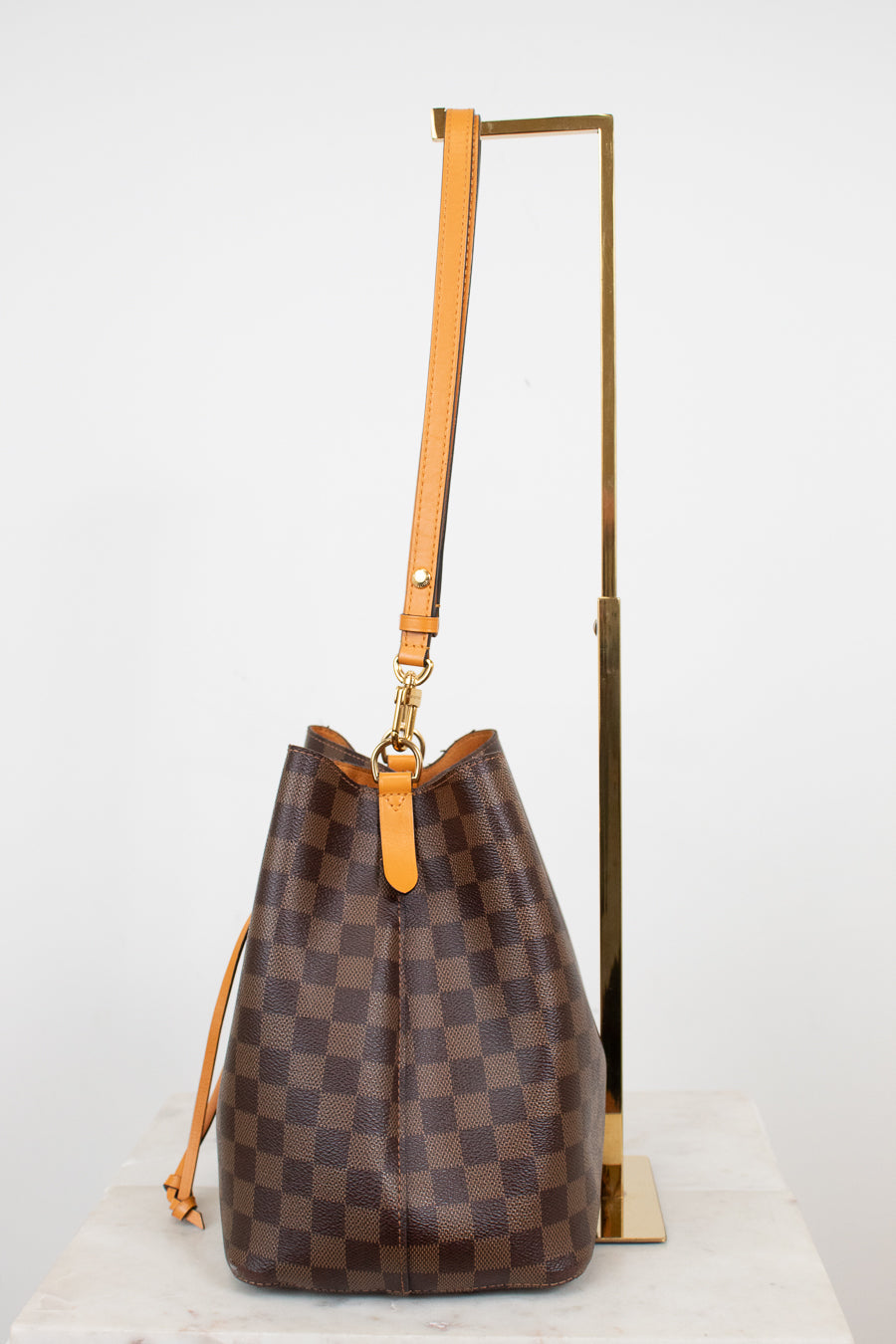 Brown checkered handbag with orange leather strap on a white background