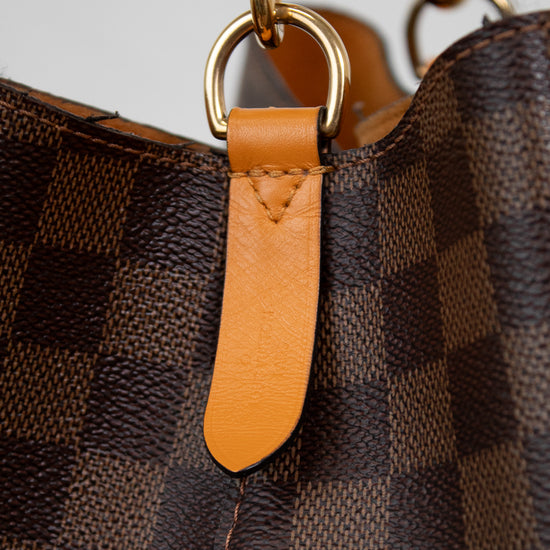 Close-up of a brown checkered handbag with gold hardware and an orange leather tag.