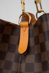 Close-up of a brown checkered handbag with gold hardware and an orange leather tag.