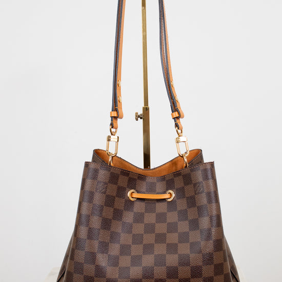 Brown checkered handbag with gold and orange accents on a white background