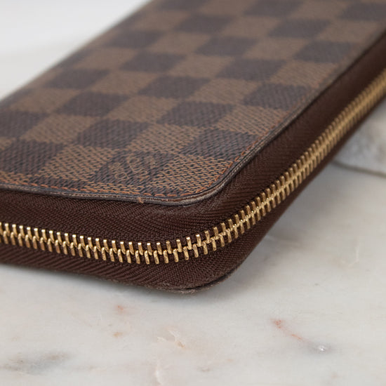 Brown checkered wallet with gold zipper on a marble surface