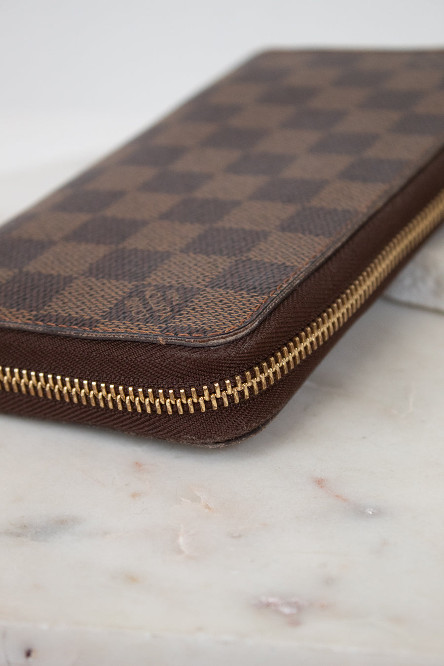 Brown checkered wallet with gold zipper on a marble surface