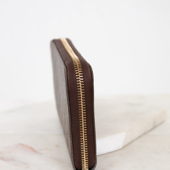 Brown wallet with gold zipper on a marble surface