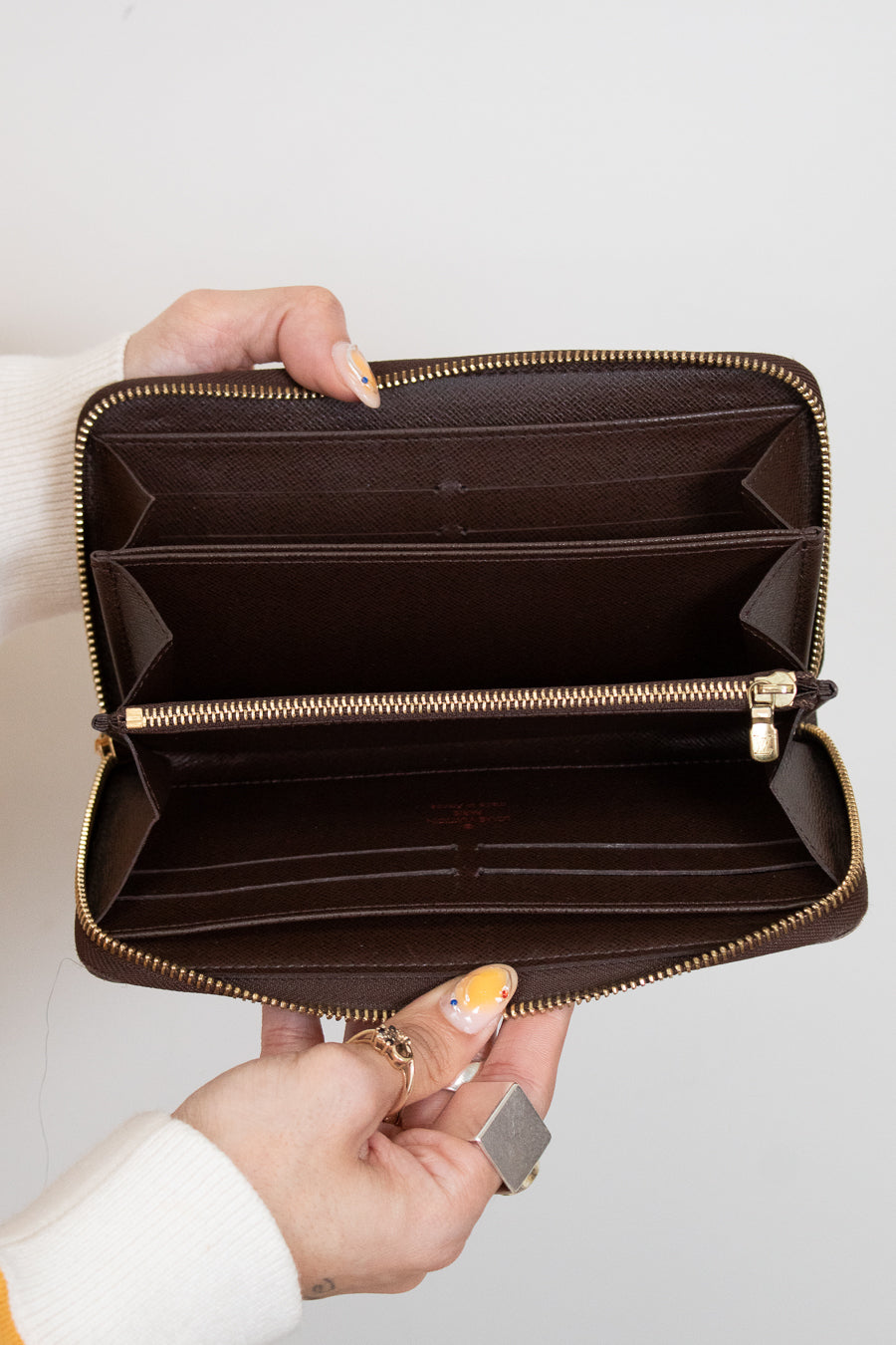 Brown wallet with gold zipper held open by a hand on a light gray background