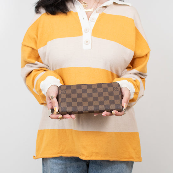 Person wearing a yellow and beige striped shirt holding a brown checkered wallet.