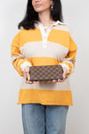 Person wearing a yellow and beige striped shirt holding a brown checkered wallet.