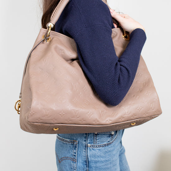 Person wearing a navy sweater and blue jeans, holding a beige handbag against a plain background