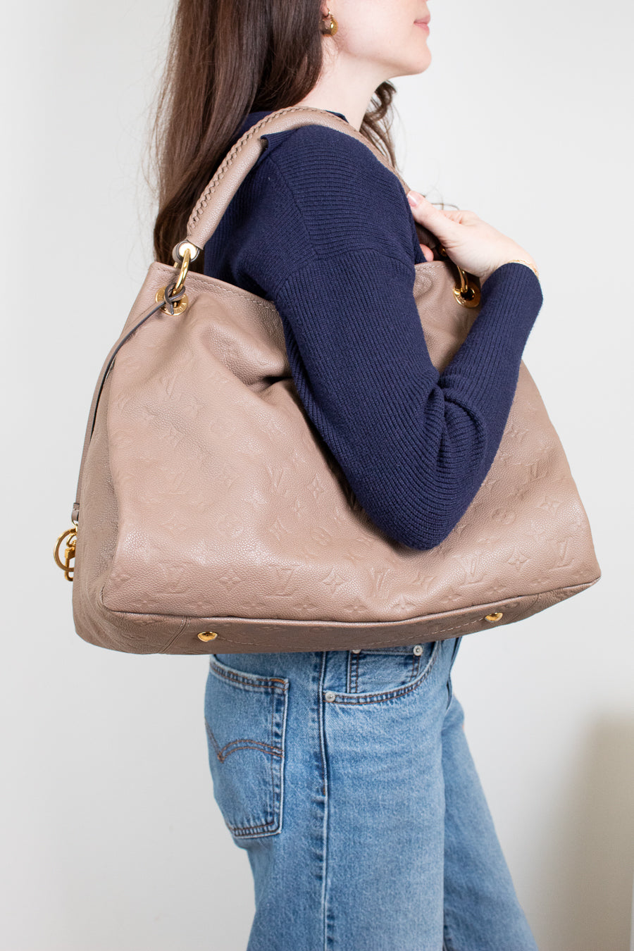 Person wearing a navy sweater and blue jeans, holding a beige handbag against a plain background
