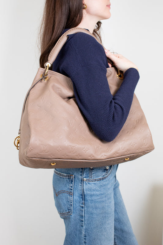 Person wearing a navy sweater and blue jeans, holding a beige handbag against a plain background