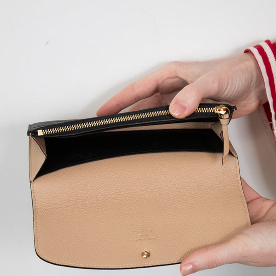 Beige interior of black wallet with gold zipper held by a hand on a light gray background
