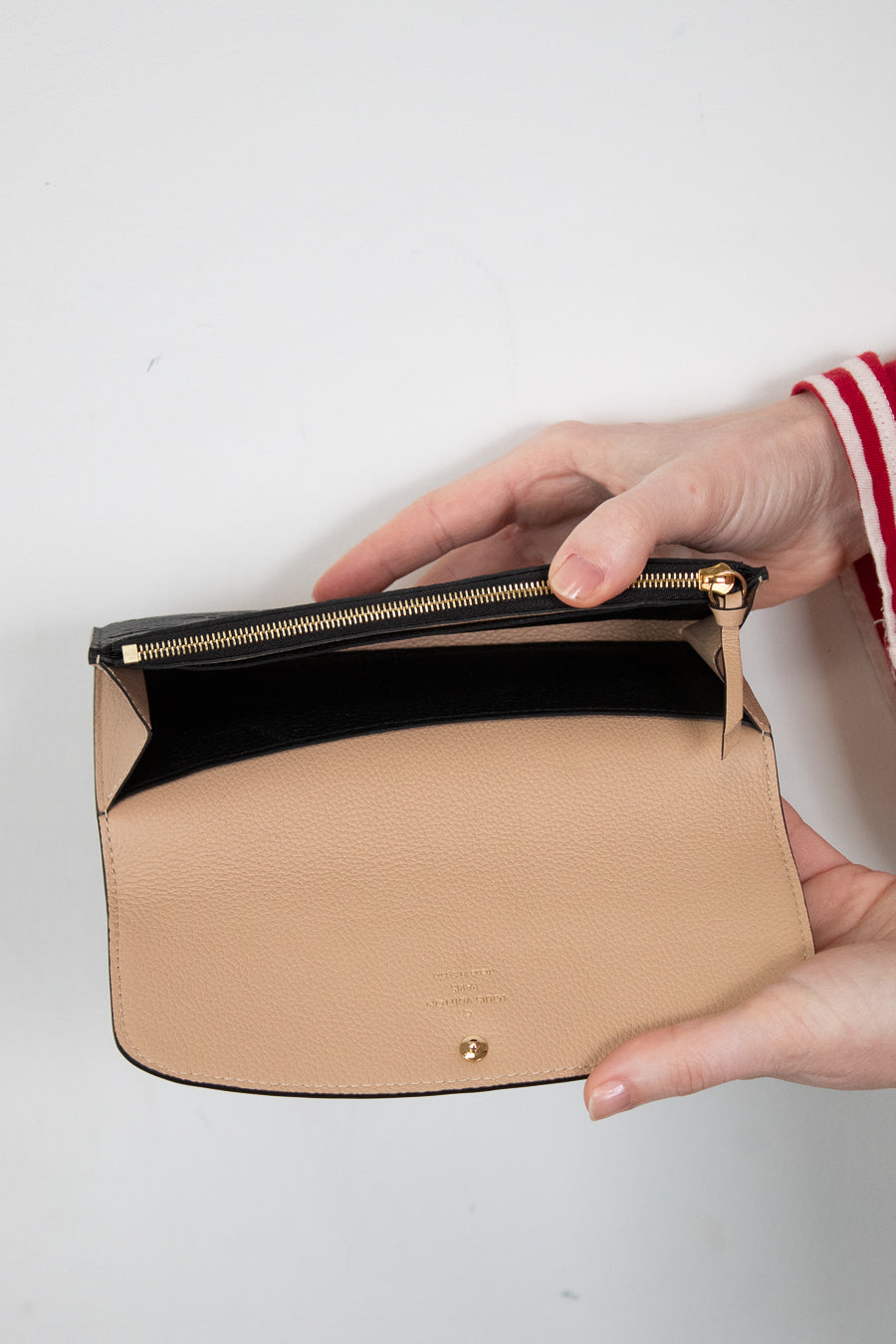 Beige interior of black wallet with gold zipper held by a hand on a light gray background