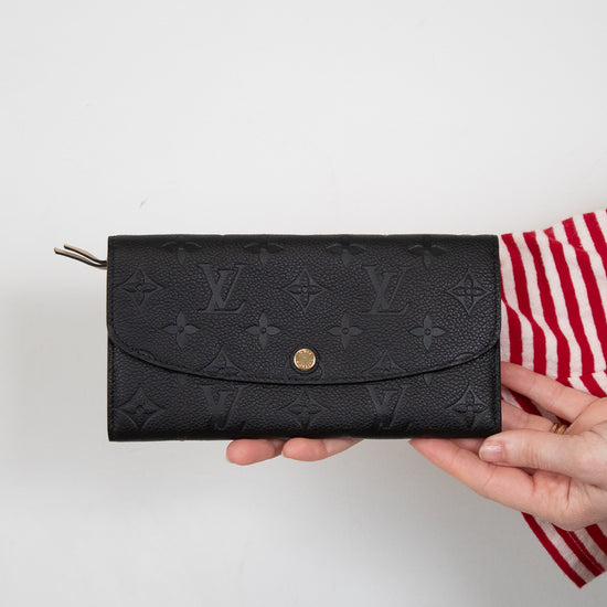 Black wallet with brand logo held by a person on a white background