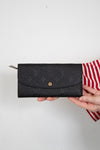 Black wallet with brand logo held by a person on a white background