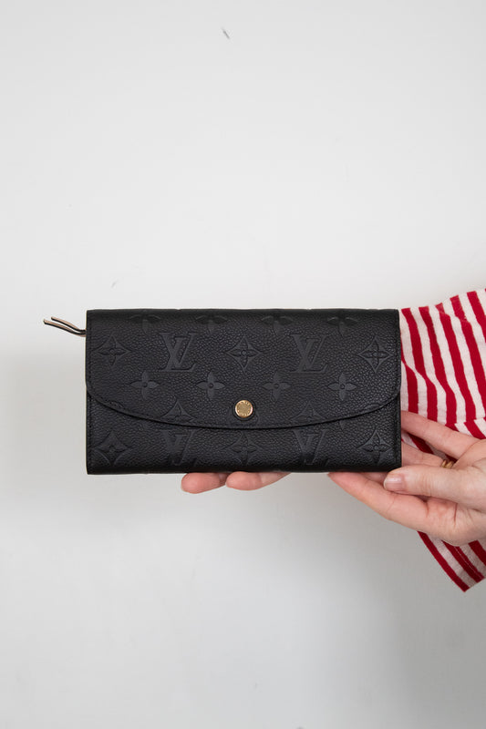 Black wallet with brand logo held by a person on a white background
