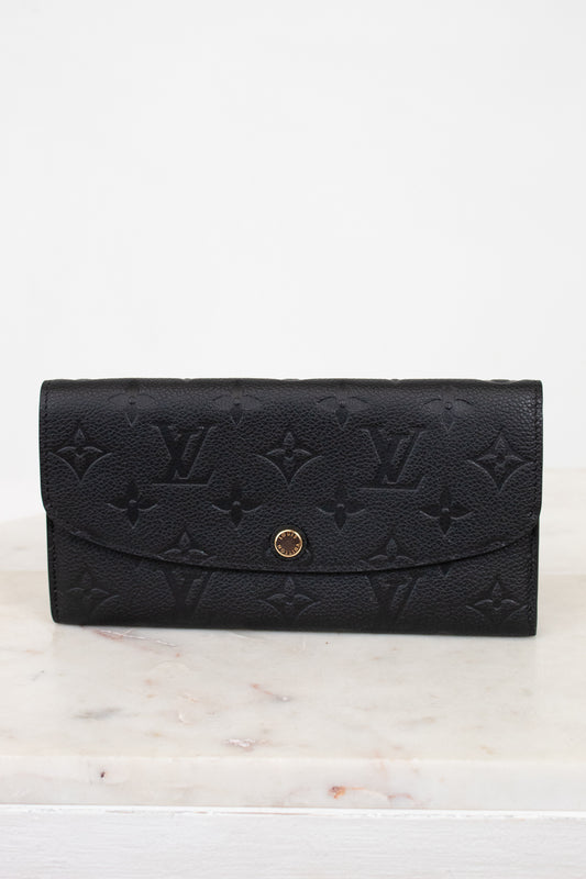 Black embossed wallet with gold clasp on a white marble surface
