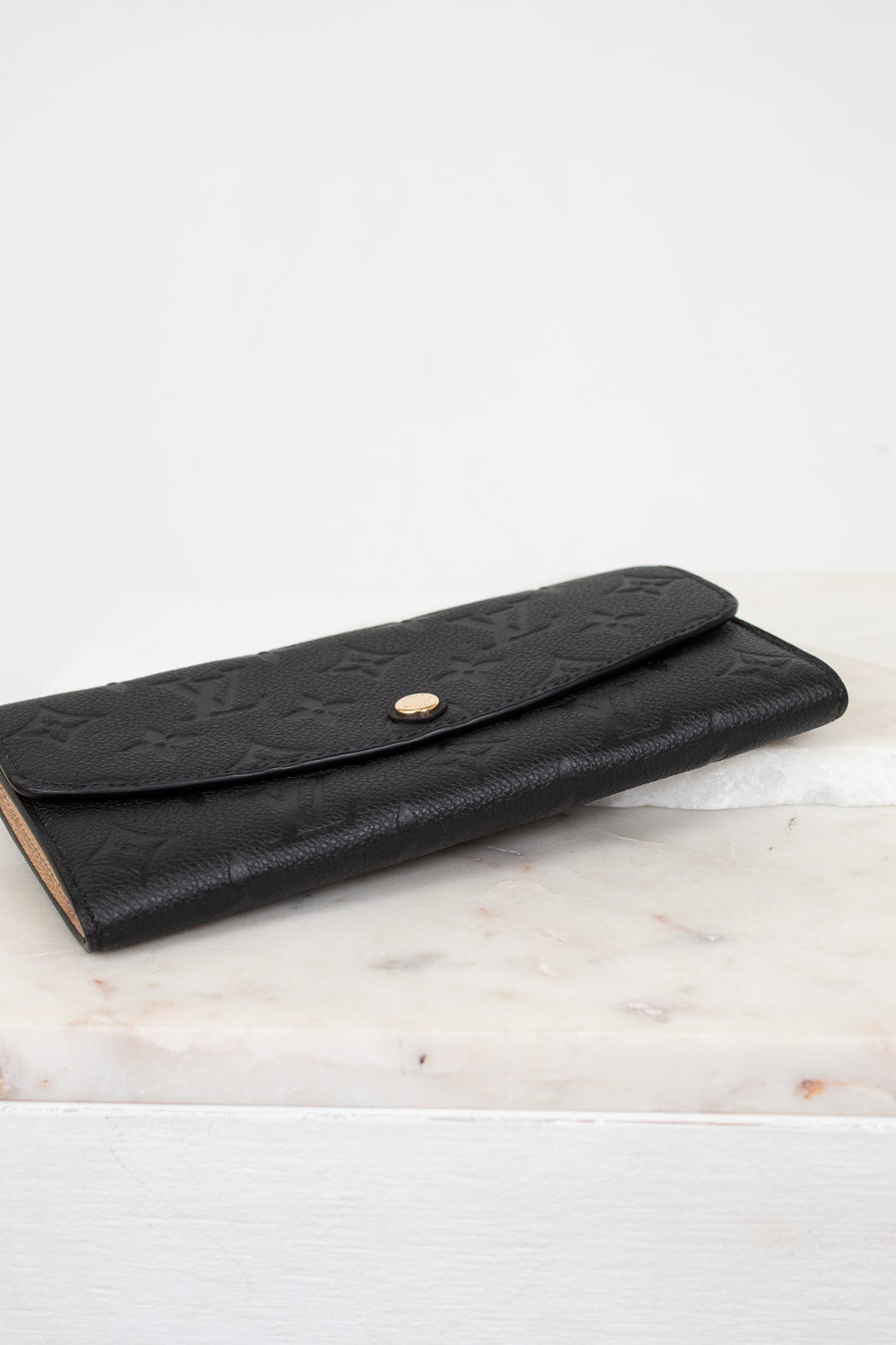 Black embossed wallet on a marble surface with a white background