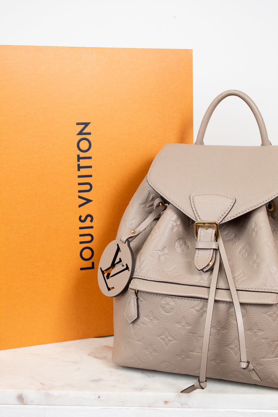 Louis Vuitton backpack with monogram pattern on a white surface with an orange Louis Vuitton box in the background.
