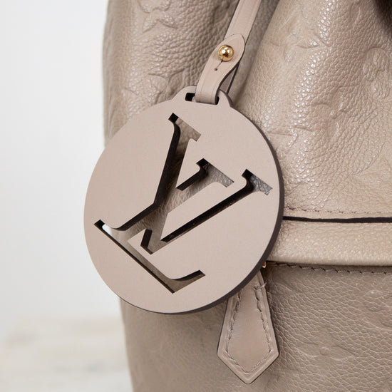 Close-up of a beige leather handbag with a prominent logo tag on a light background