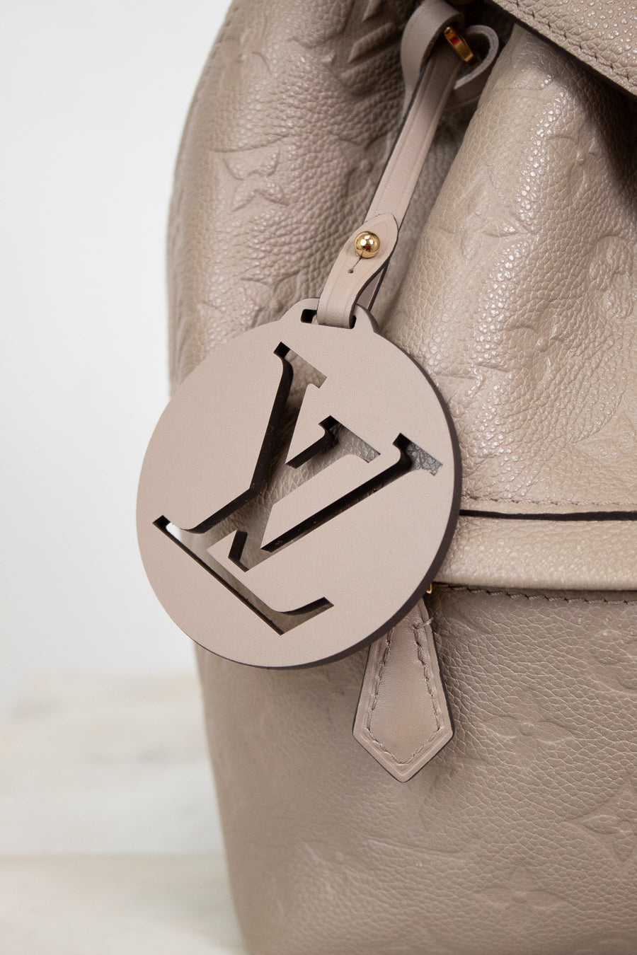 Close-up of a beige leather handbag with a prominent logo tag on a light background