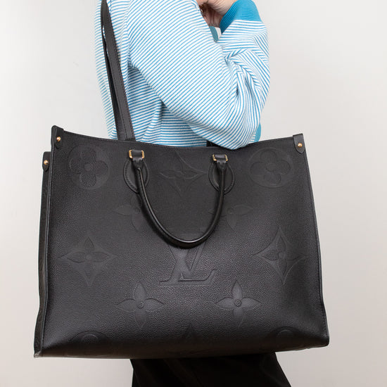 Person holding a black leather handbag with a brand logo against a white background