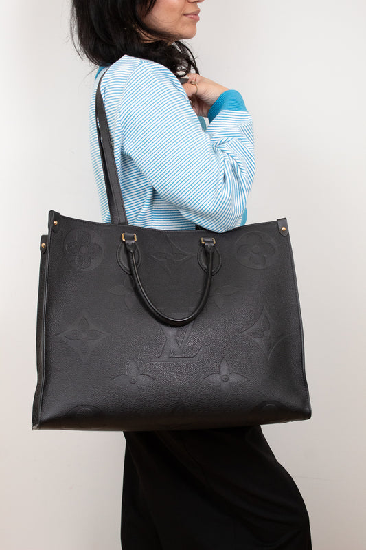 Person holding a black leather handbag with a brand logo against a white background