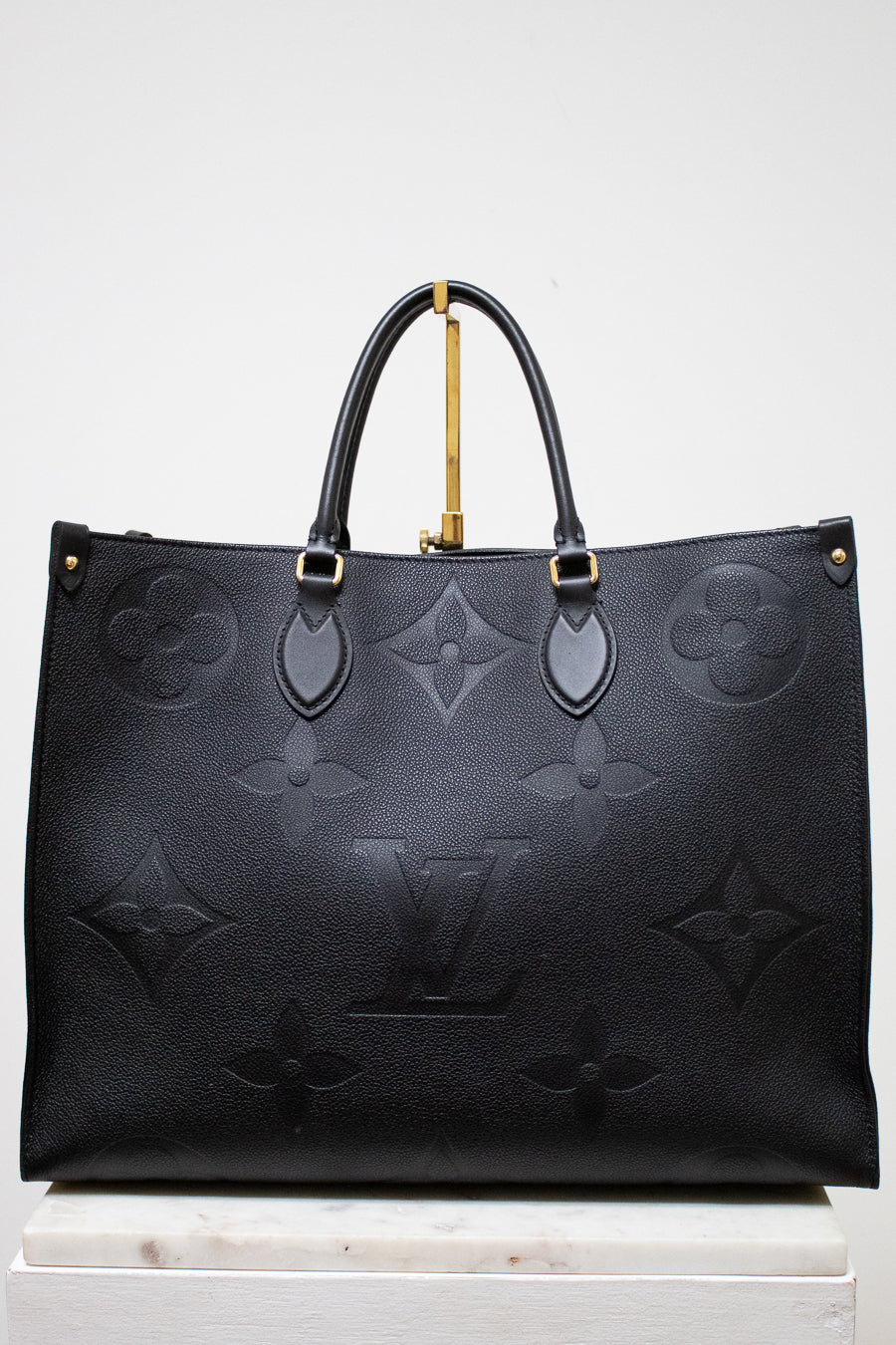 Black embossed handbag with gold accents on a white background