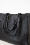 Black leather handbag with embossed design on a light gray background