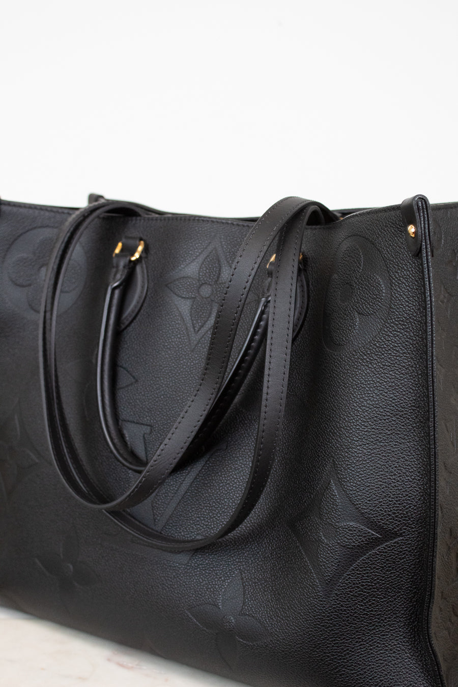 Black leather handbag with embossed design on a light gray background