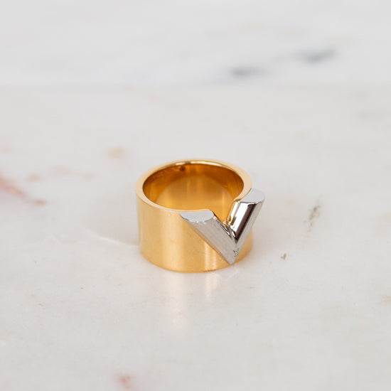 Gold ring with a silver 'V' on a marble surface