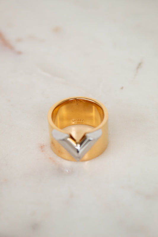 Gold ring with a unique silver V design on a light marble background