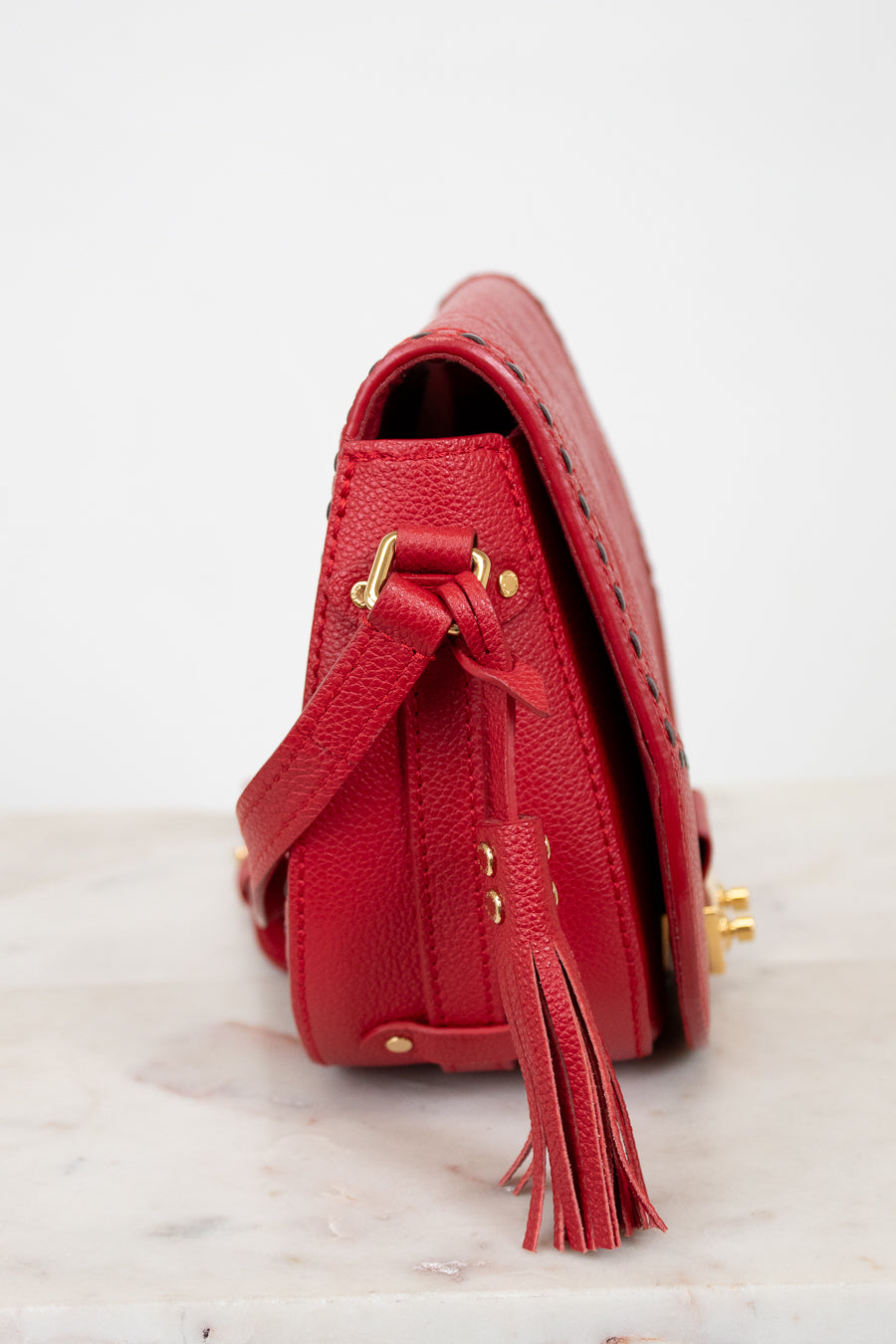 Red handbag with gold accents and a tassel on a white background