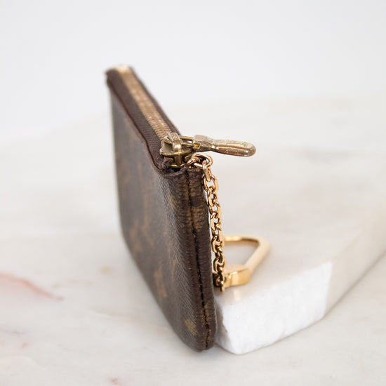 Small brown key pouch with gold chain on a white marble surface