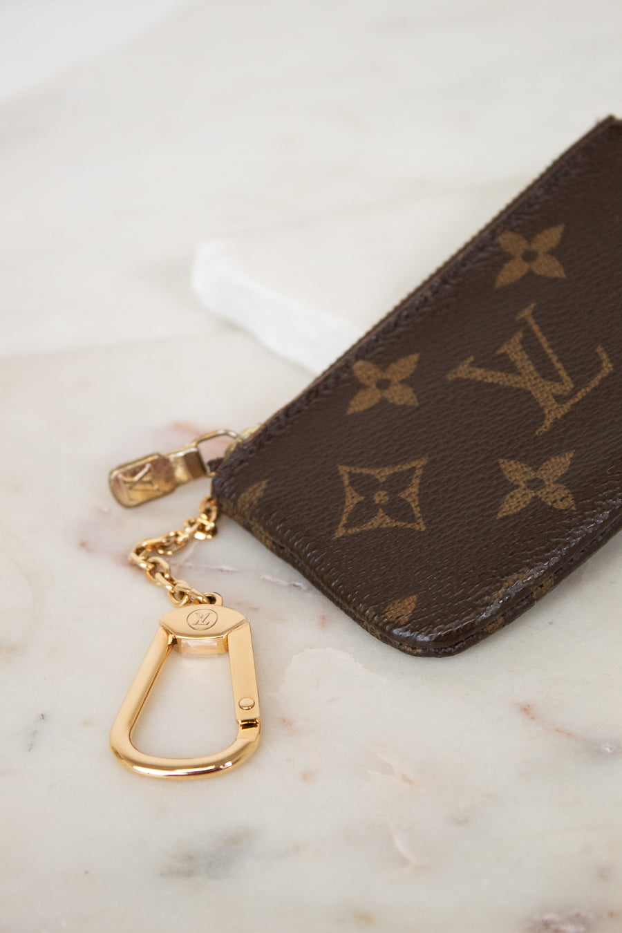 Louis Vuitton key pouch with gold chain on a marble surface