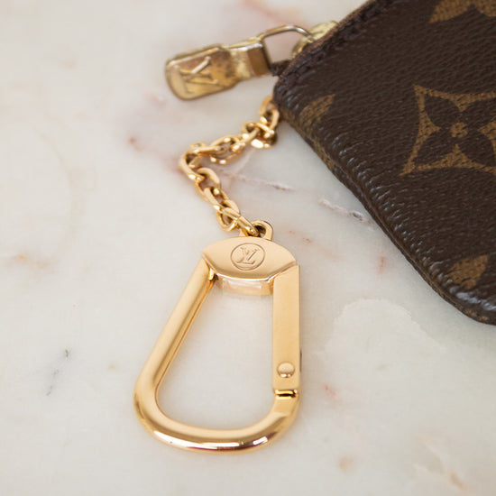 Gold keychain attached to a brown Louis Vuitton pouch on a marble surface