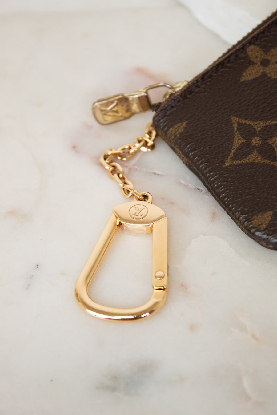 Gold keychain attached to a brown Louis Vuitton pouch on a marble surface